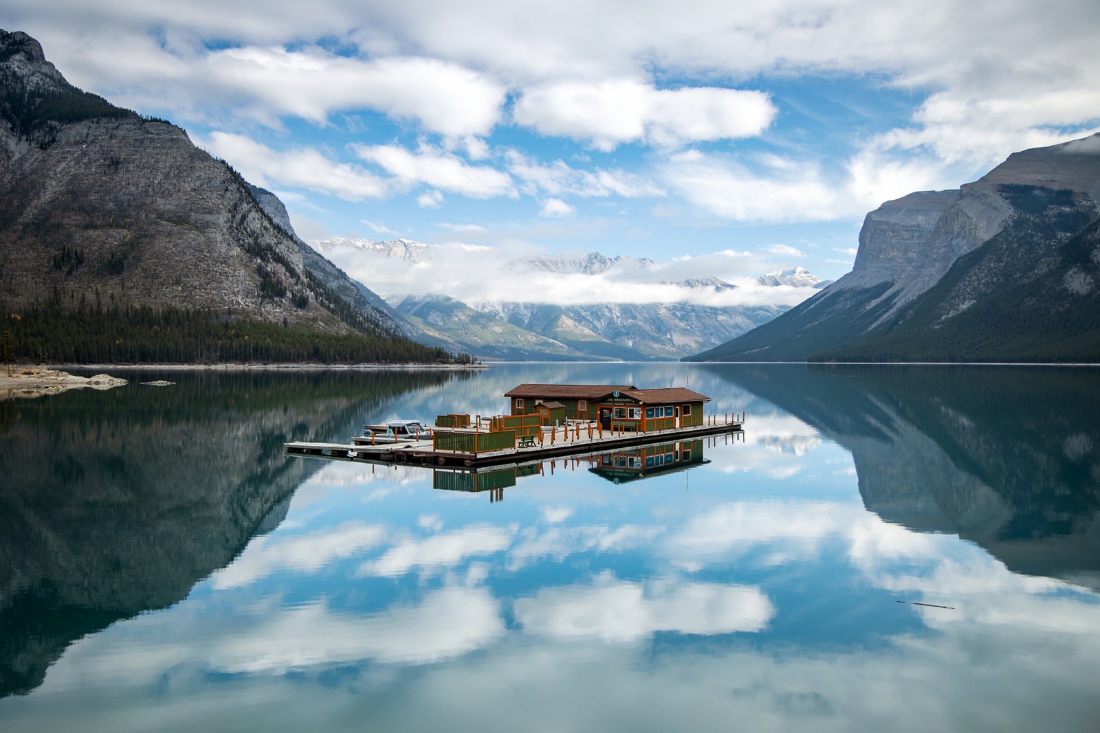 Le lac Minnewanka calme comme un miroir, avec son hangar à bateaux sur un quai flottant