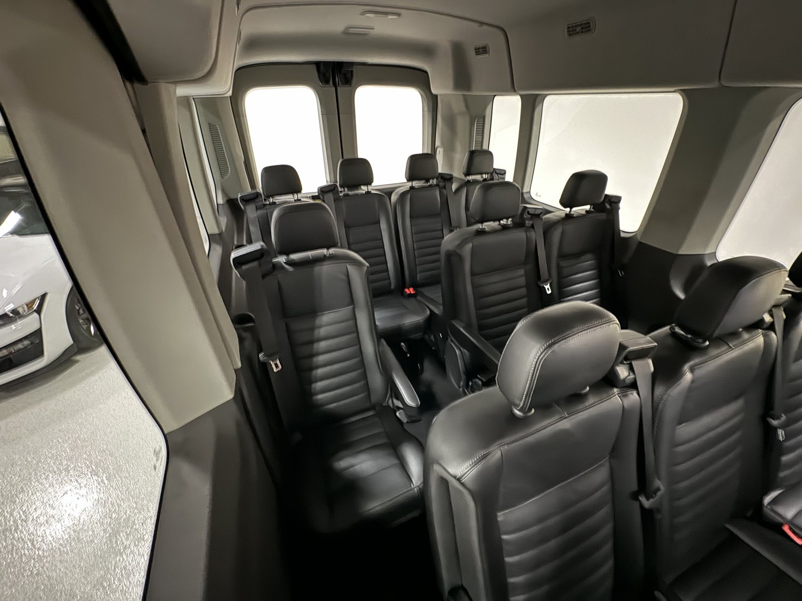 L’intérieur d’une Ford Transit 12 passagers : rangées de sièges en cuir noir vues de l’arrière