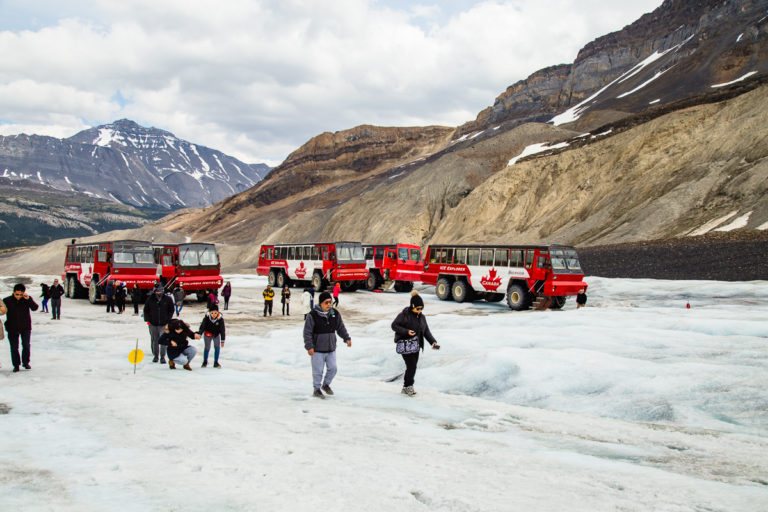 Des visiteurs marchent sur le glacier Athabasca, près des véhicules d’exploration rouges
